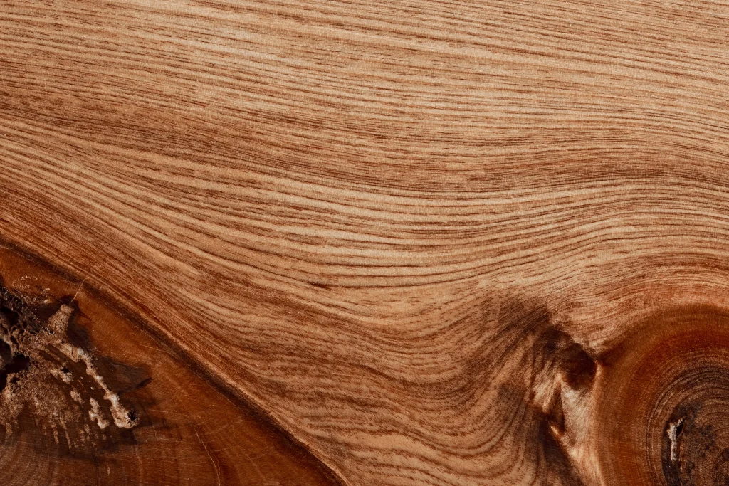 Close-up of natural hardwood with warm brown tones, flowing grain patterns, and visible knots.